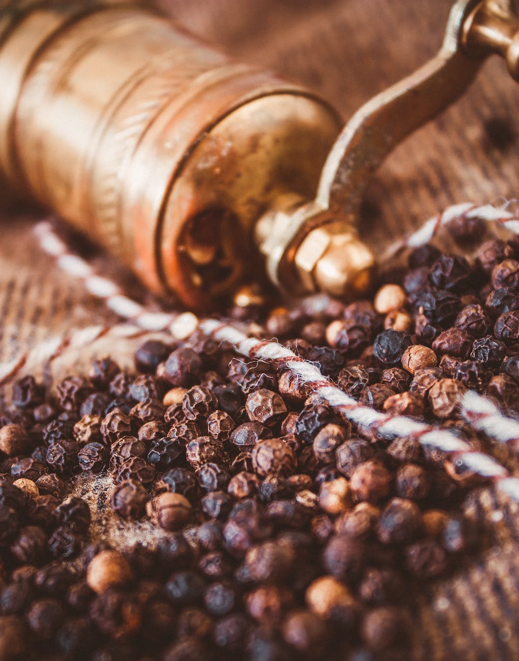 black peppercorns lying next to brass grinder