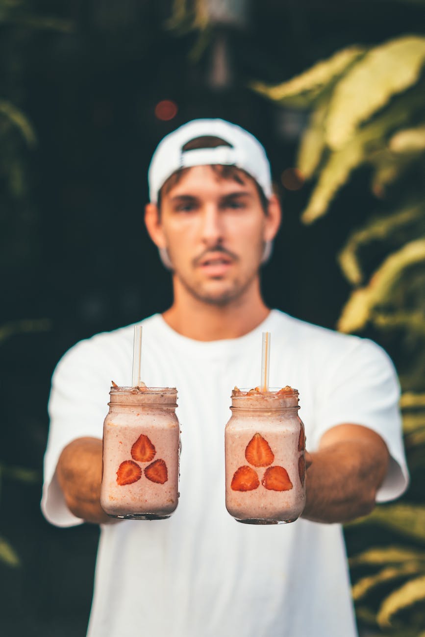 man wearing white crew neck t shirt and fitted cap holding two glass jars