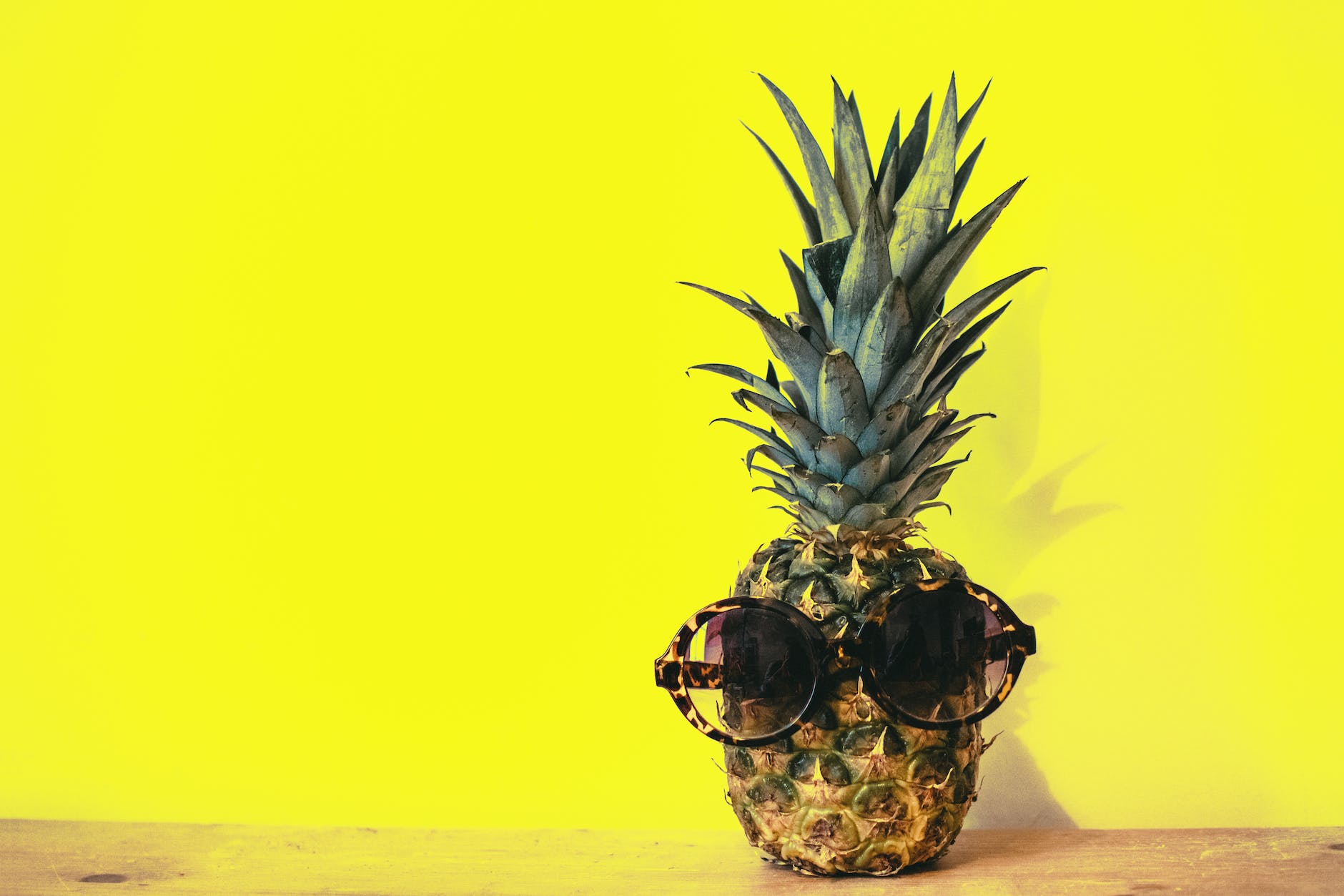 green pineapple fruit with brown framed sunglasses beside yellow surface