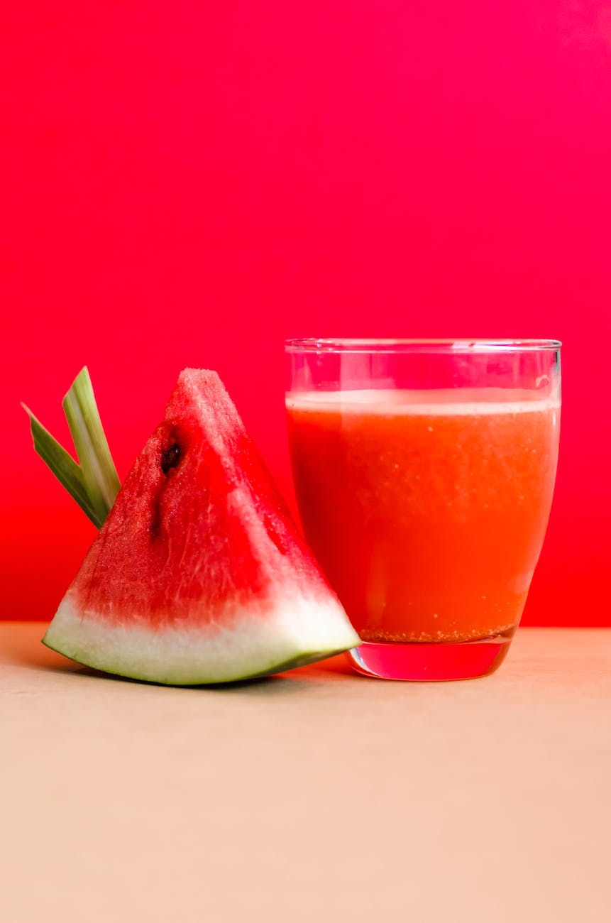 watermelon shake filled glass cup beside sliced watermelon fruit on brown surface