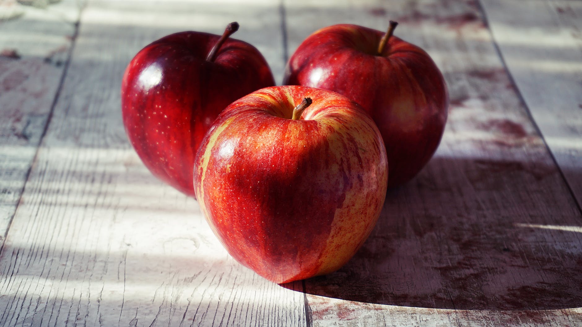 three red apples on wooden surface