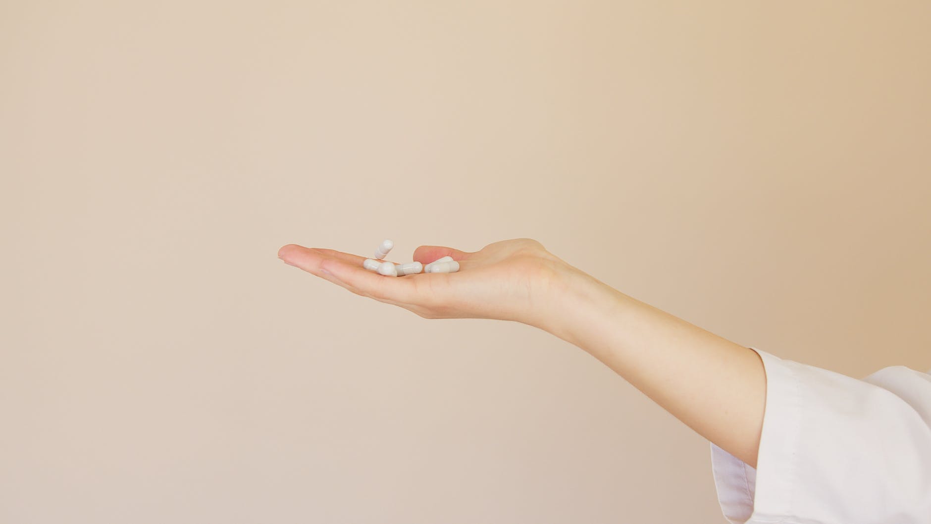 crop female pharmacist with pile of white pills on palm