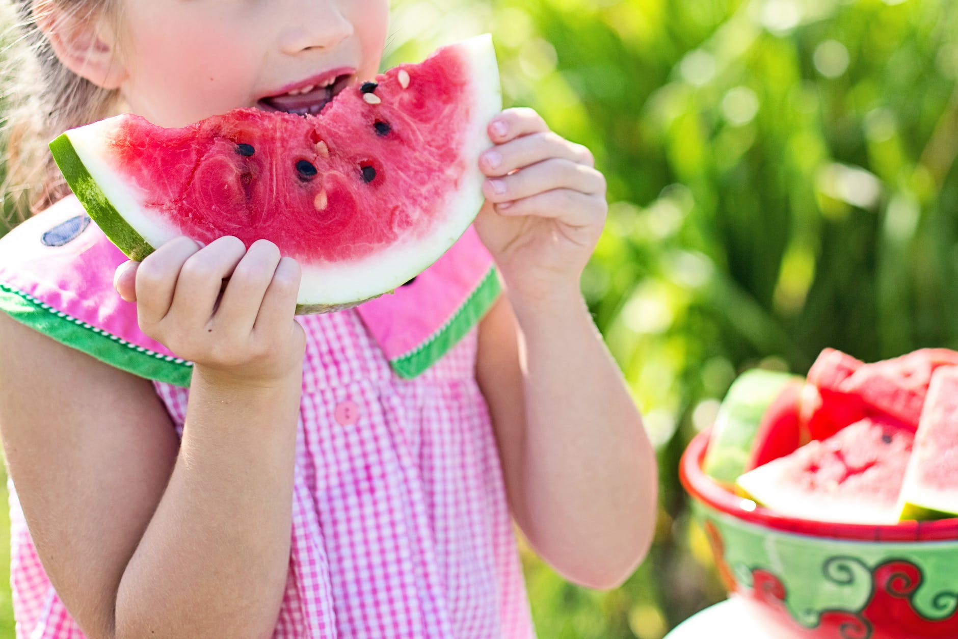 girl eating sliced watermelon fruit beside table