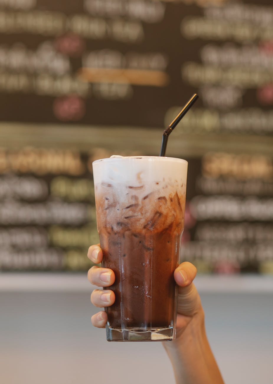 crop faceless woman raising glass of iced coffee latte