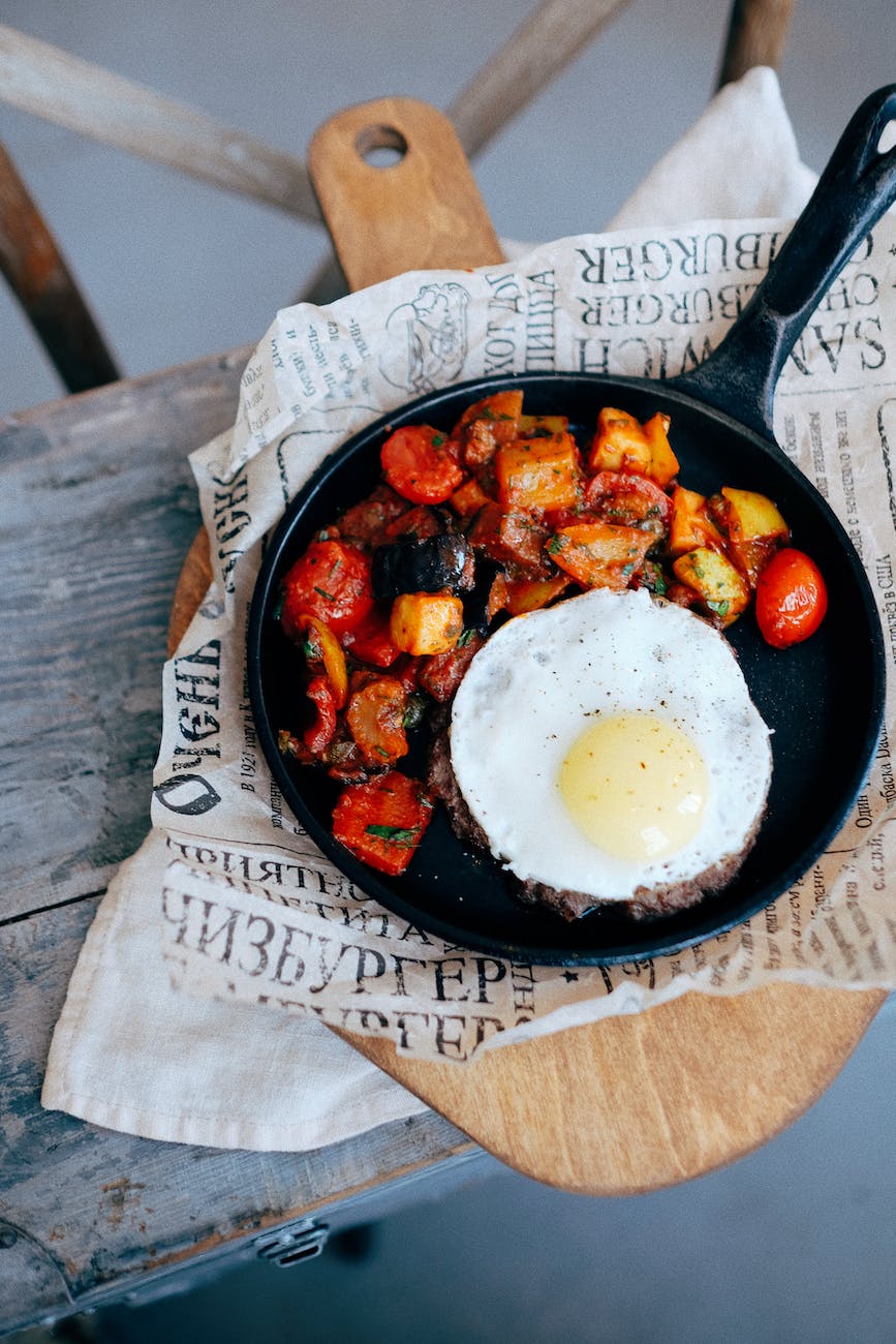 pan with roasted vegetables and steak with egg placed on wooden board