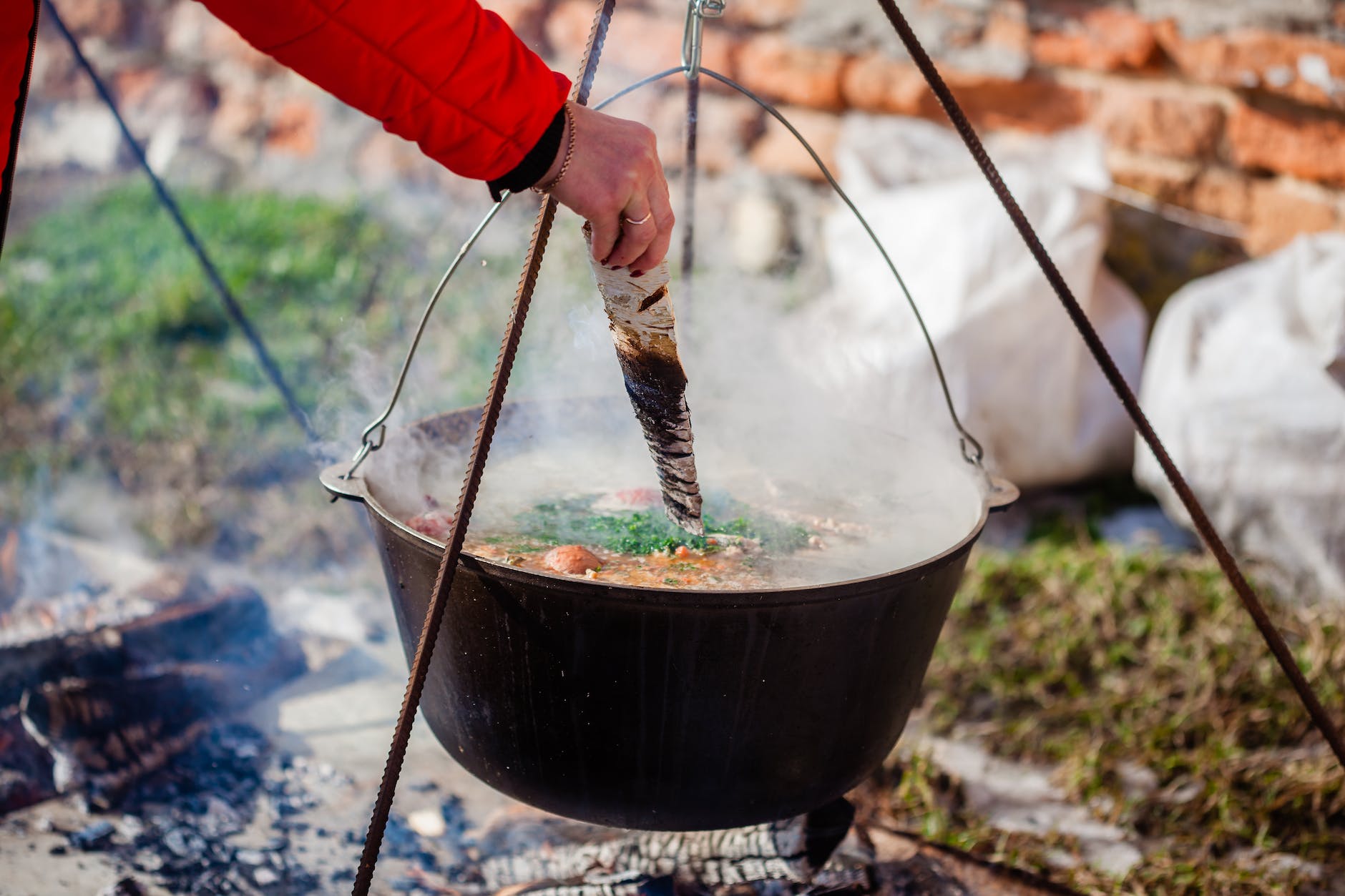 crop person with cut wood preparing fish soup in pot